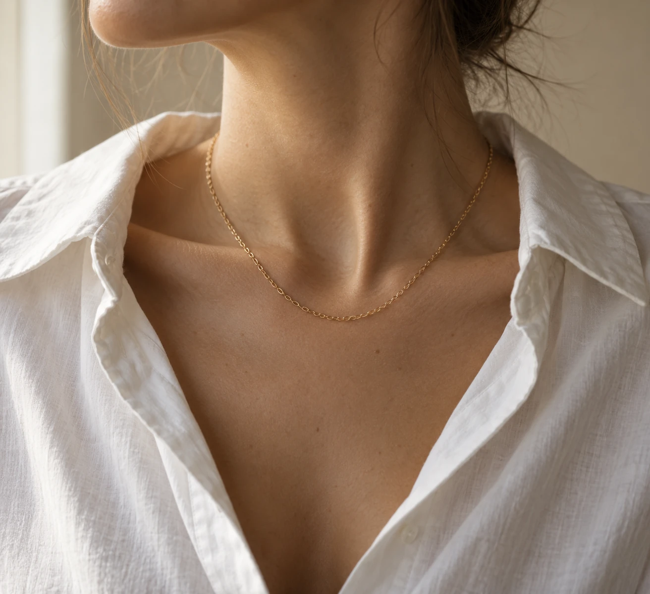 Close crop of a neck and open-collar white shirt with a single fine gold chain, illustrating a simple everyday necklace look.