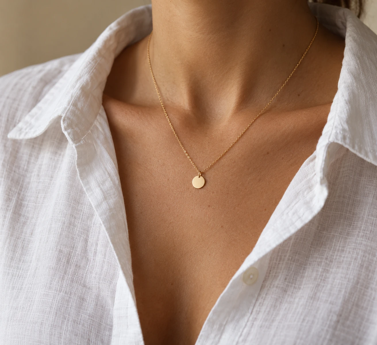 Close crop of an open-collar white linen shirt with a single fine gold chain and one small round pendant.