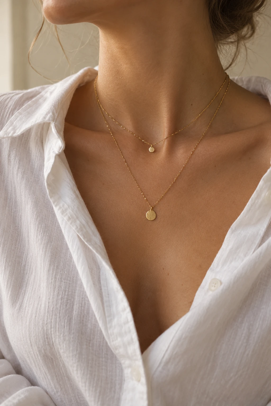 Vertical close crop of an open-collar white shirt with two fine gold chains at different lengths.