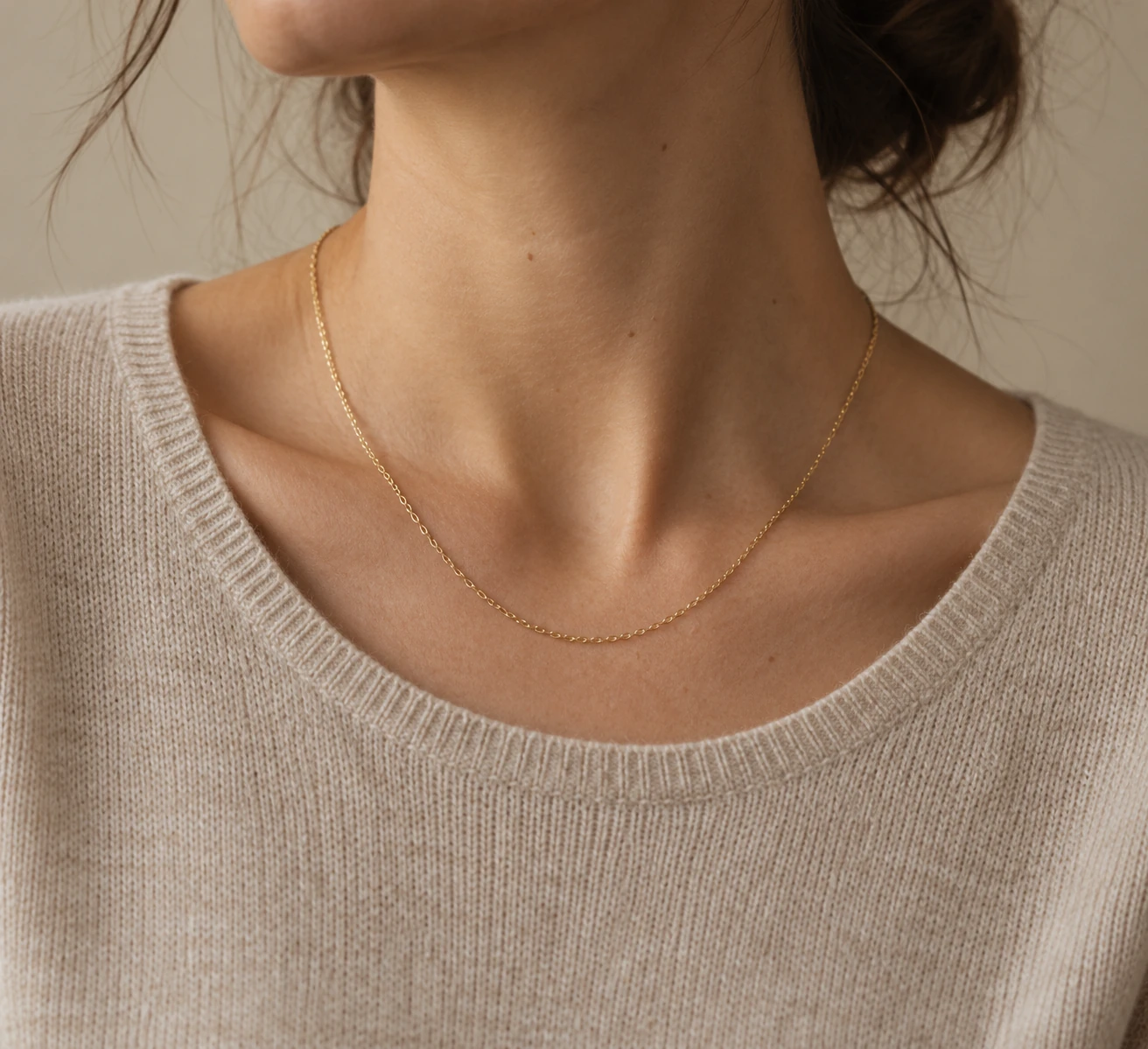 Close crop of an oatmeal fine knit worn with one simple fine gold chain and no pendant.